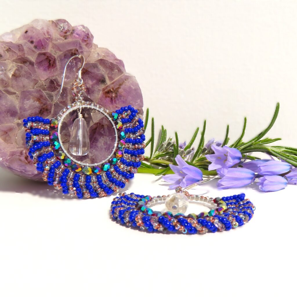 Statement swirl hoop earrings with Miyuki seed beads on silver toned hoops with a large clear Quartz drop suspended in the centre.  Set on sterling silver ear wires.  Designed and crafted by Fiona of Fifi and the Peacock
