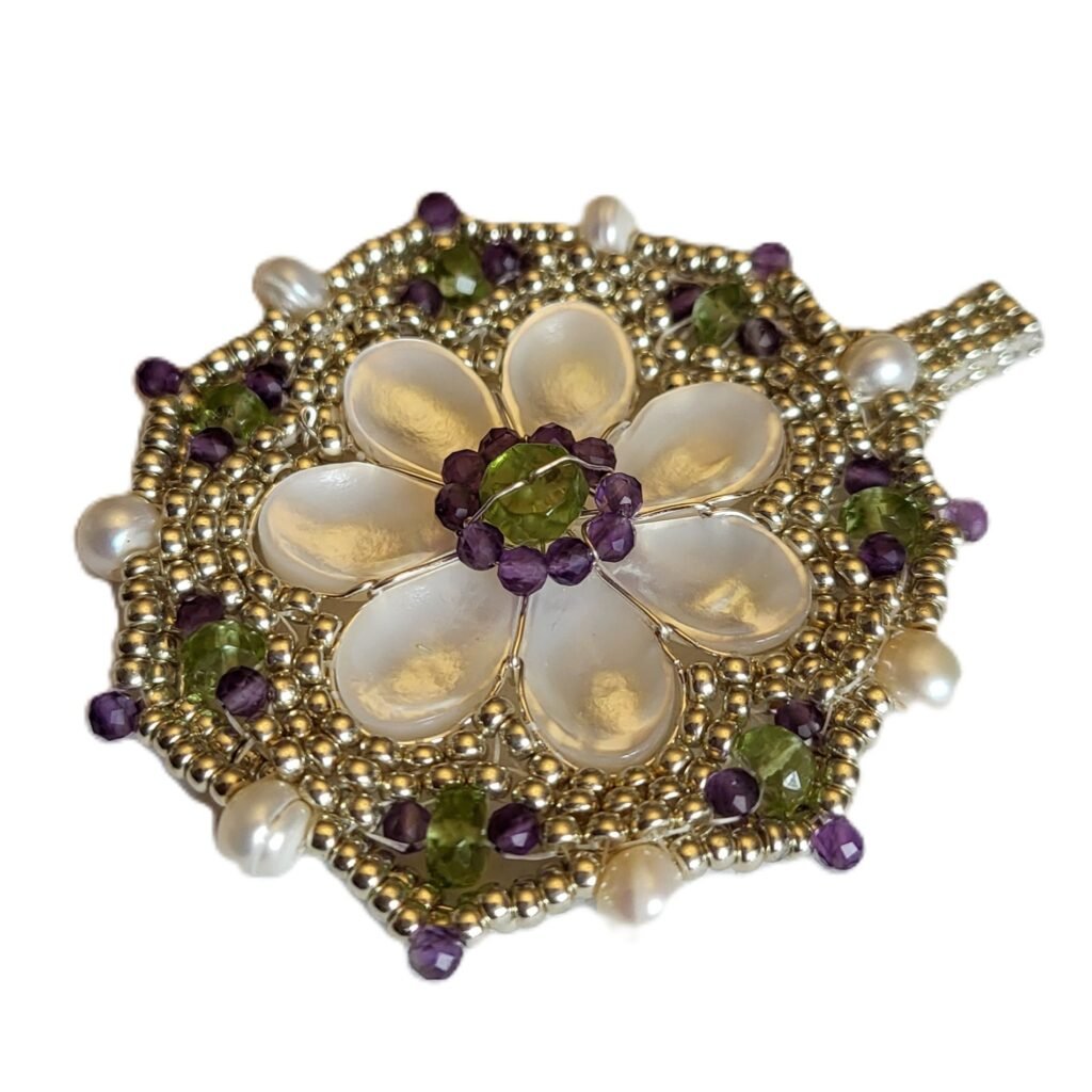Pendant featuring a mother of pearl central flower in a Miyuki seed bead frame work featuring Peridot, Amethyst and Cultured Freshwater Pearls.  This piece was designed to sit alongside other pieces commissioned by the returning customer featuring the same gemstones